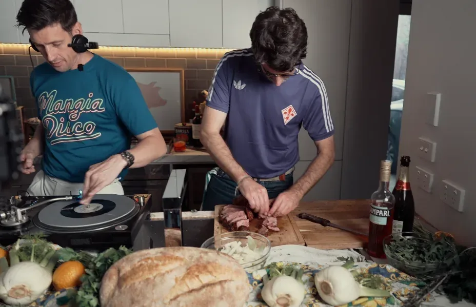 Andy mixing records while Matt carves bistecca alla fiorentina in the Mangia Disco kitchen